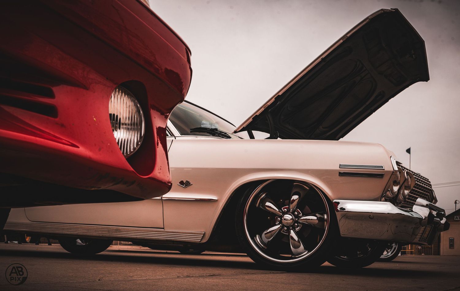 Low-angle view of a white classic car with hood open beside a red vintage automobile.
