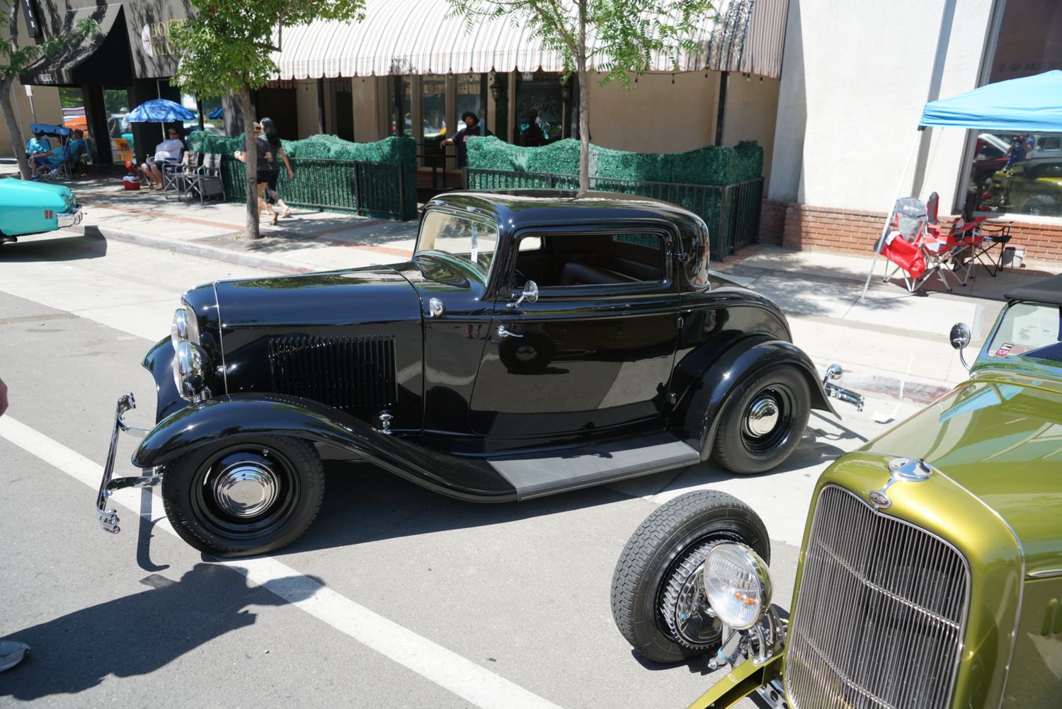 Classic black 1932 Ford three-window coupe hot rod parked at a sunny street car show.