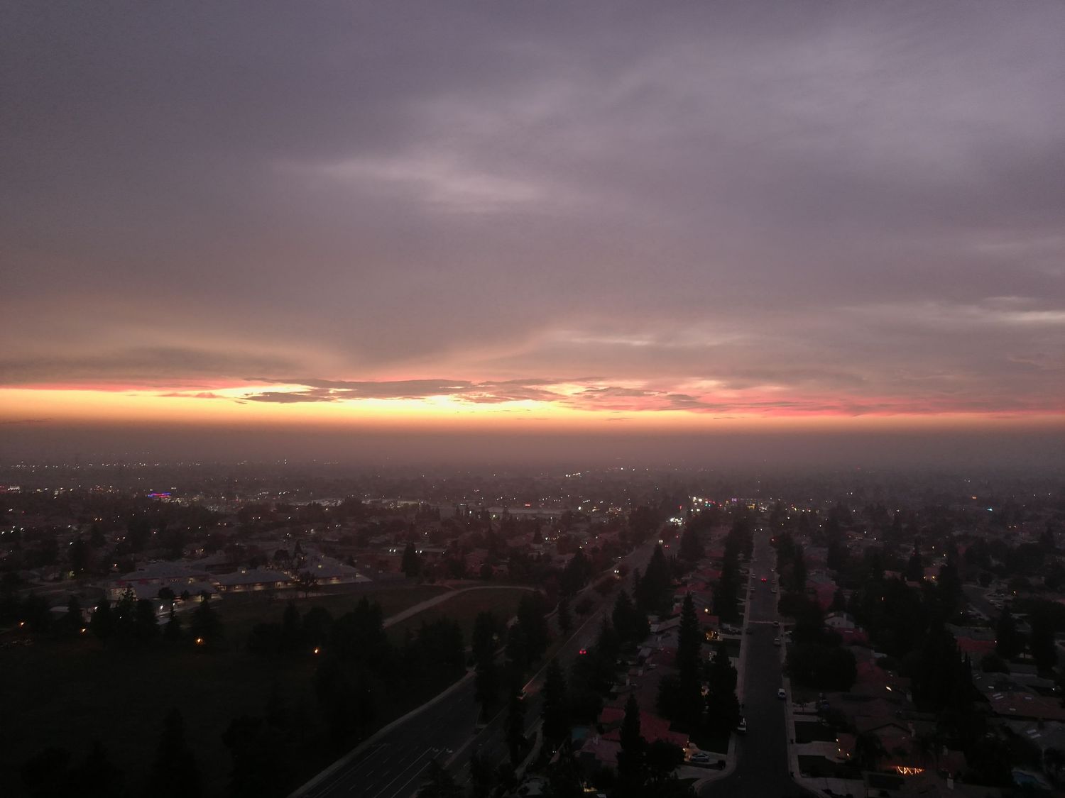 Aerial view of a sprawling city at dusk with pink and purple clouds glowing on the horizon.