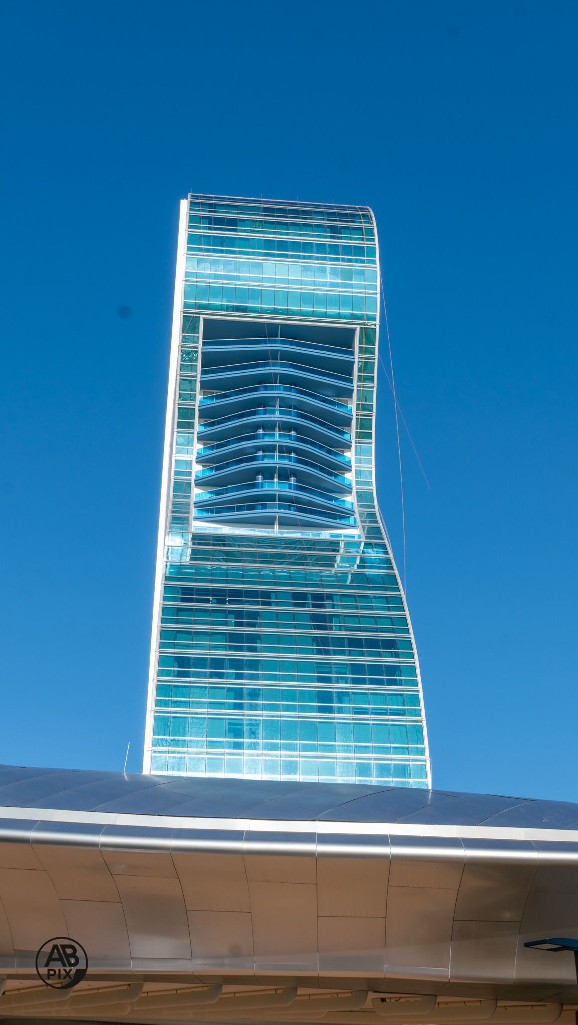 Close-up of undulating blue glass facade of contemporary twisted skyscraper against clear sky.
