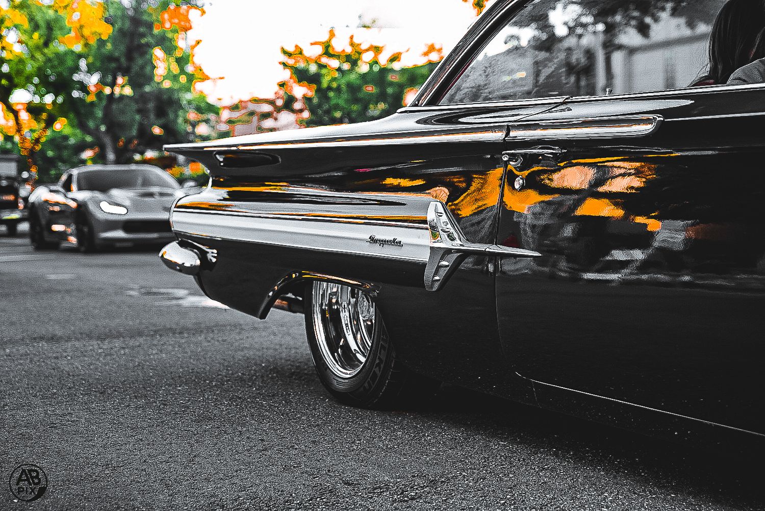 Close-up of a classic black lowrider car with chrome trim and custom wheels on a city street.