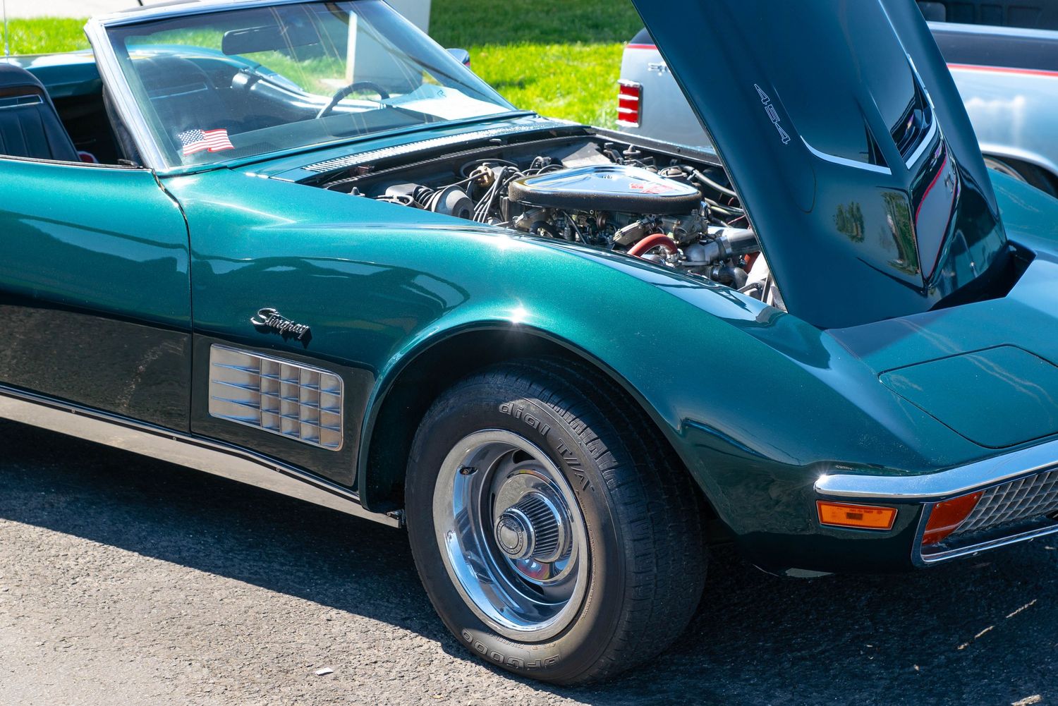 Classic green Corvette Stingray convertible with hood open revealing engine at an outdoor car show.