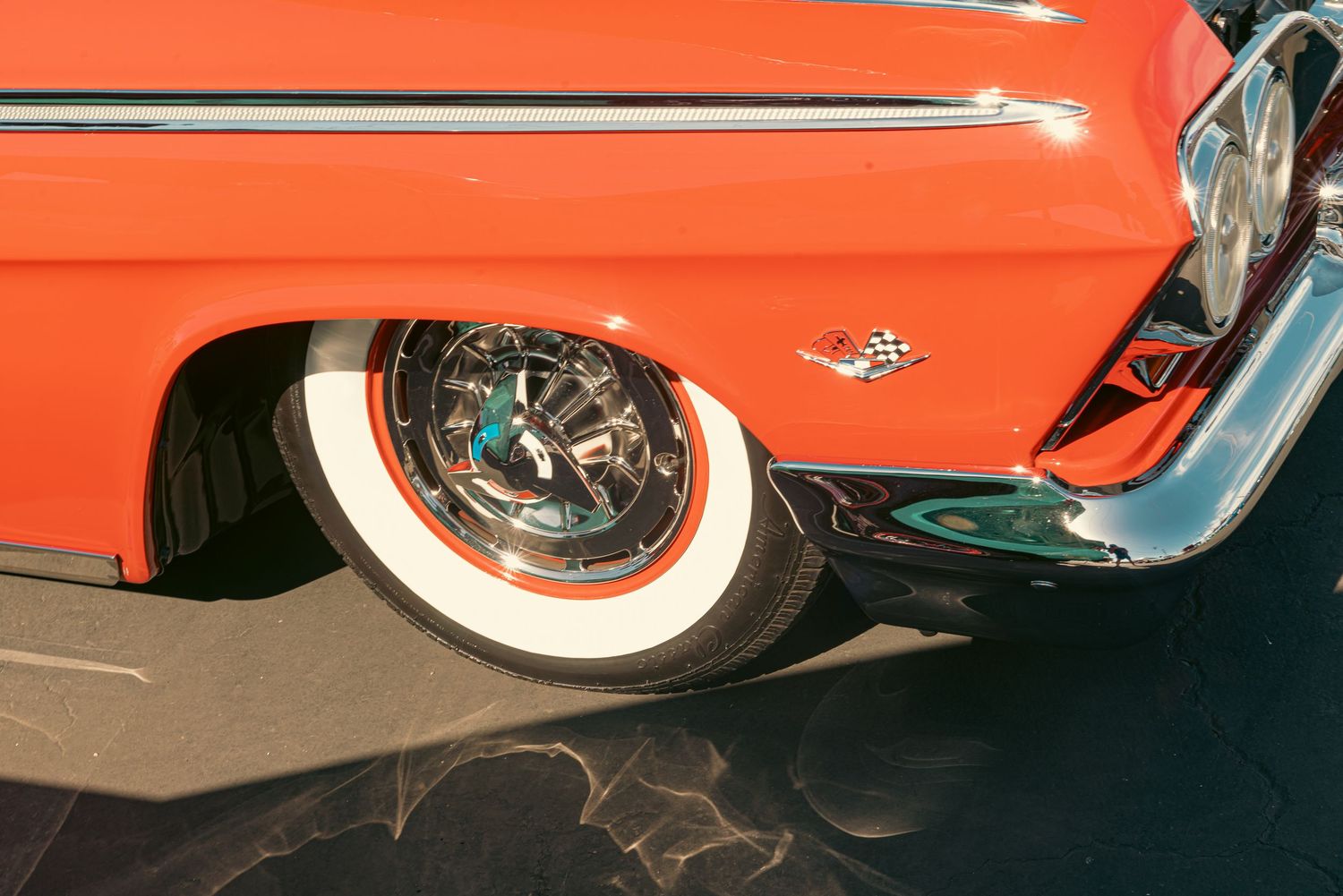 Vintage red Chevrolet classic car with chrome details, whitewall tires, and decorative hubcaps on dark pavement.