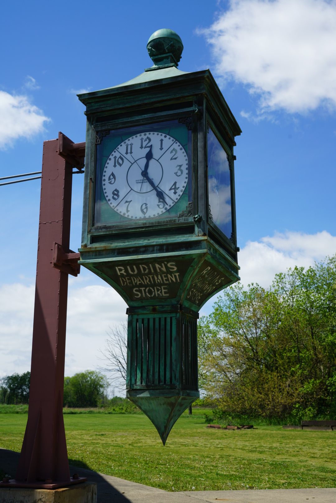 A vintage green patina clock from Rubin's Department Store stands on a red metal post under blue sky.