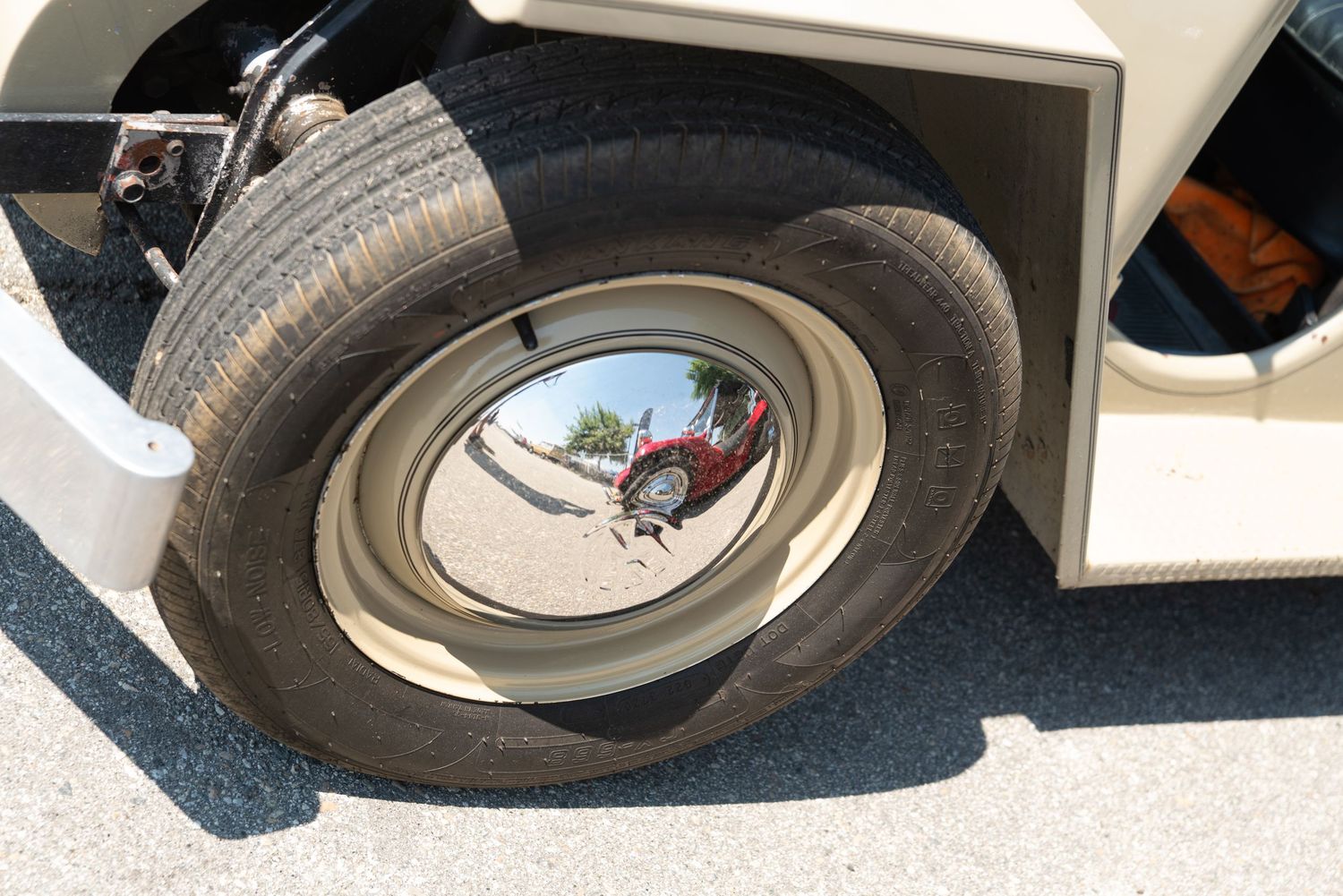 White vintage vehicle wheel with chrome hubcap reflecting surroundings on a sunny day.