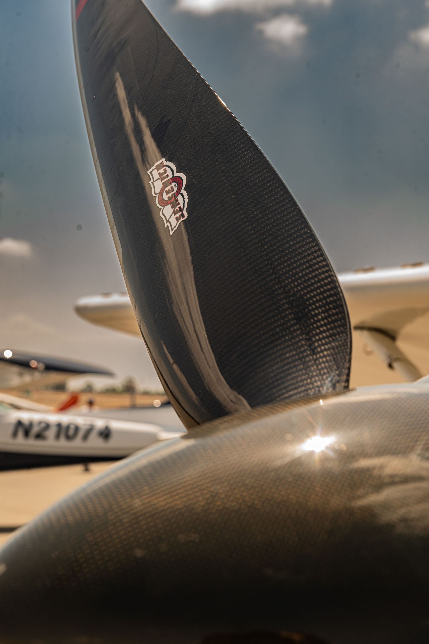 Close-up of a carbon fiber aircraft propeller blade on a small plane with registration N21074 visible in background.