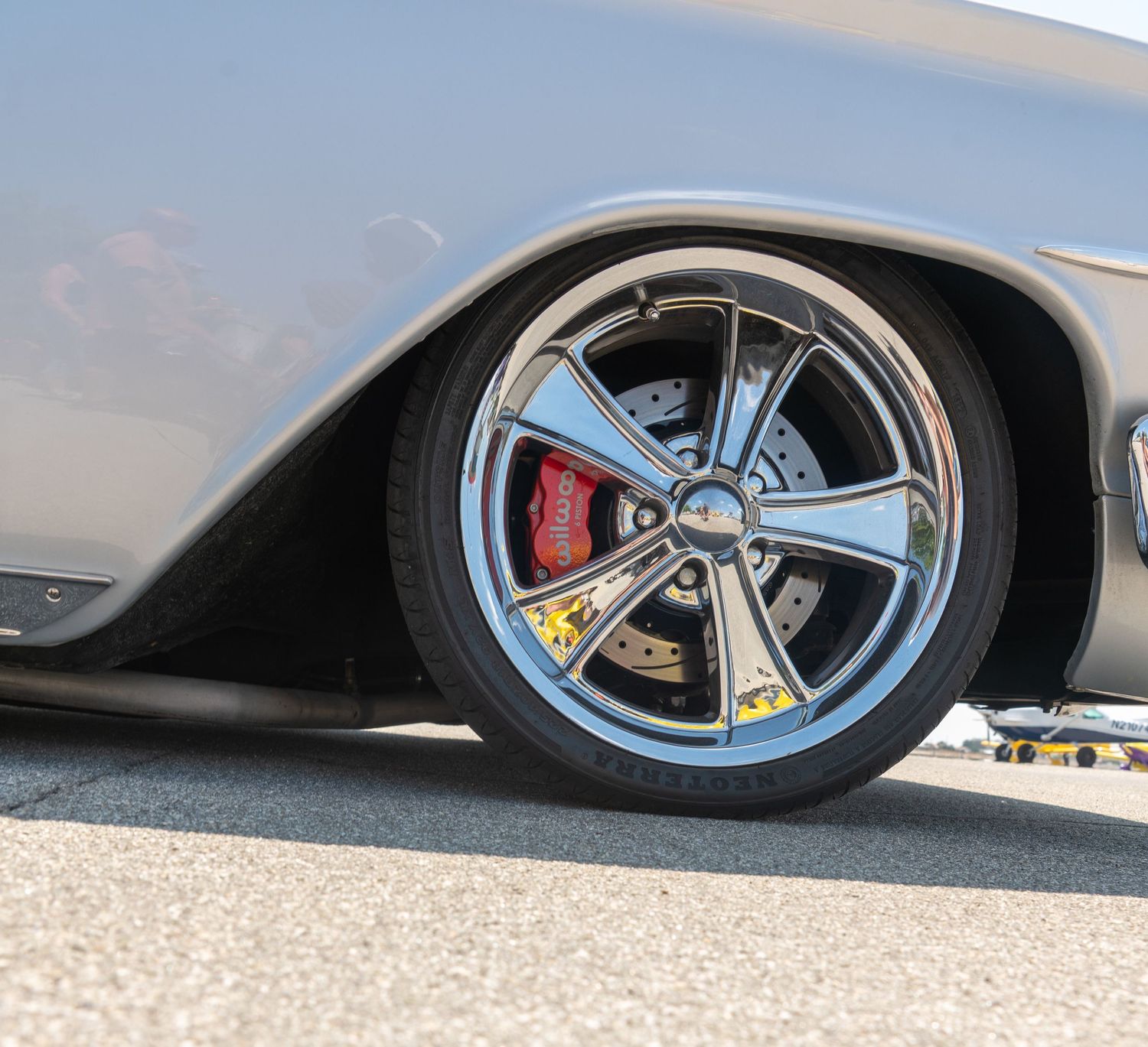 Chrome five-spoke wheel with red brake caliper on a lowered silver custom classic car.