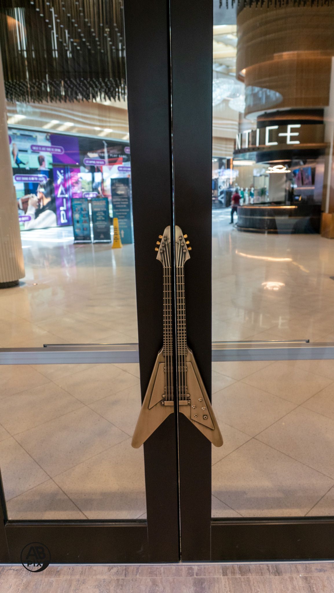 Guitar-shaped door handle on glass door inside modern entertainment venue.