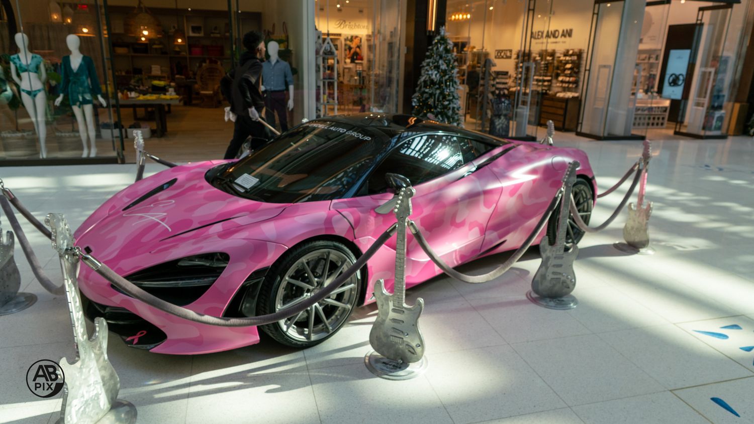 Pink McLaren 720S supercar on display inside upscale shopping mall.