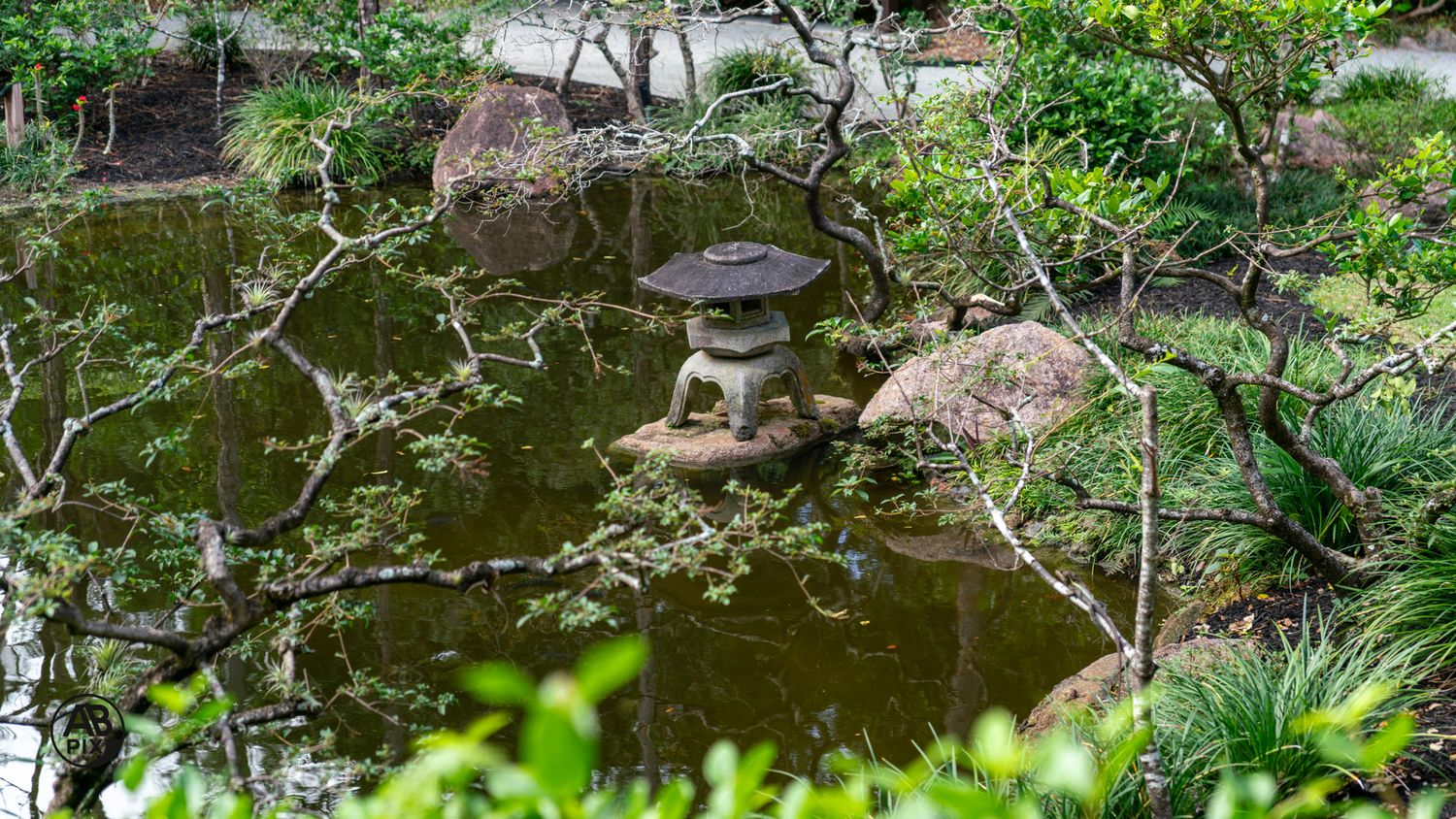 Stone pagoda lantern on small island in a Japanese garden pond surrounded by lush greenery.