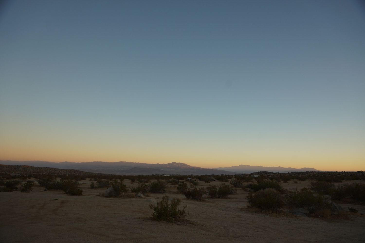 Vast desert landscape at dusk with distant mountains and sparse scrub brush.