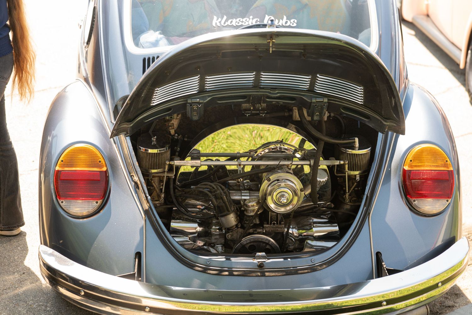 Rear engine compartment of a classic blue Volkswagen Beetle with trunk open at a car show.