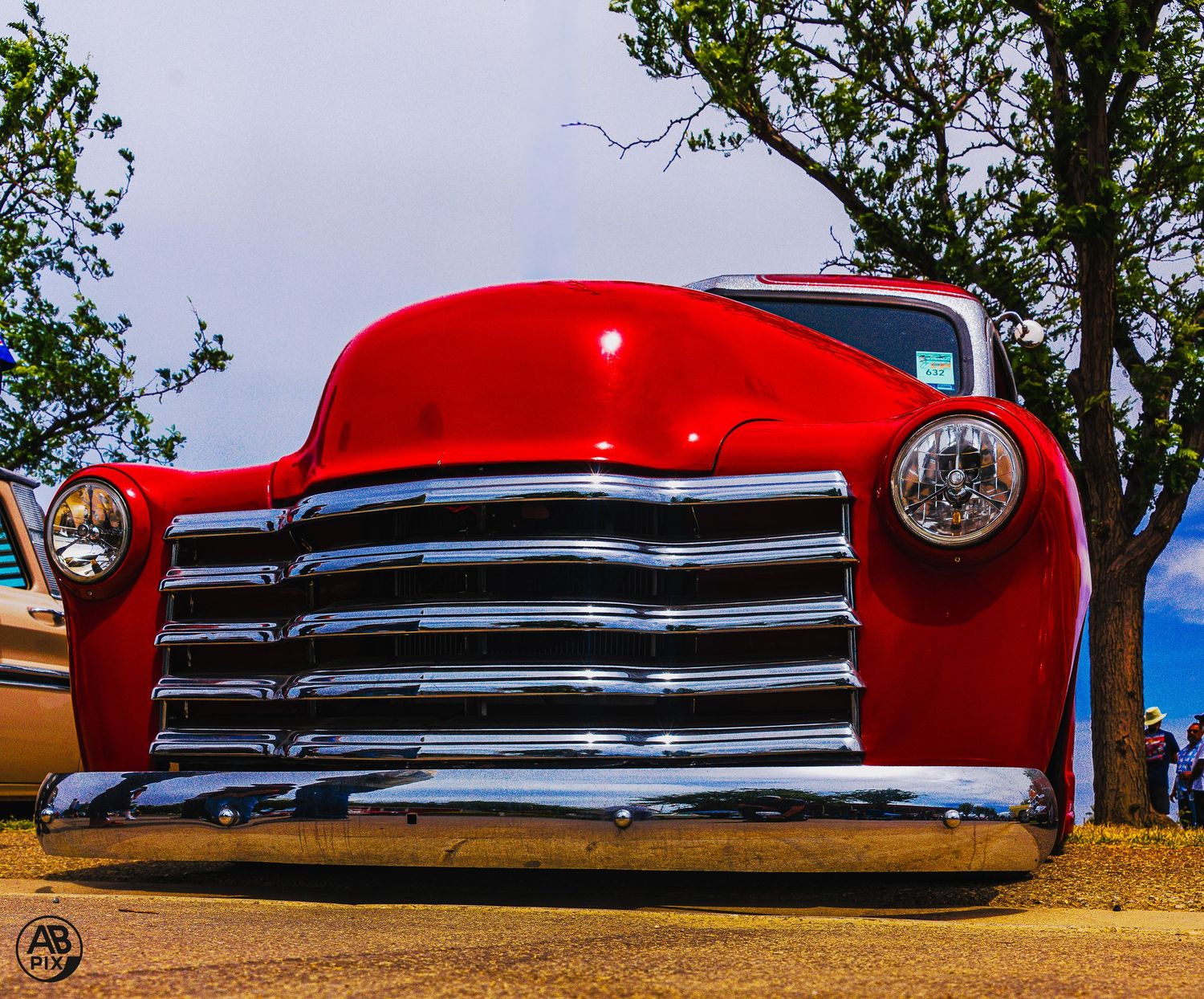 Red classic Chevrolet truck with chrome grille, low angle front view against cloudy sky.
