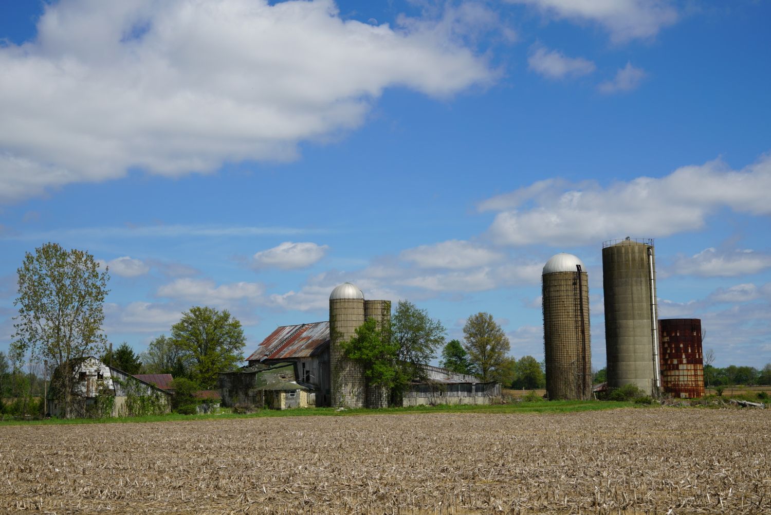 Classic Ohio farm with multiple grain silos, old barns, and freshly plowed field under blue sky.