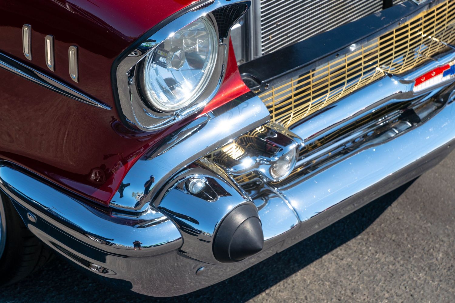 Close-up of a restored 1957 Chevrolet Bel Air in burgundy with polished chrome bumper and gold grille detail.