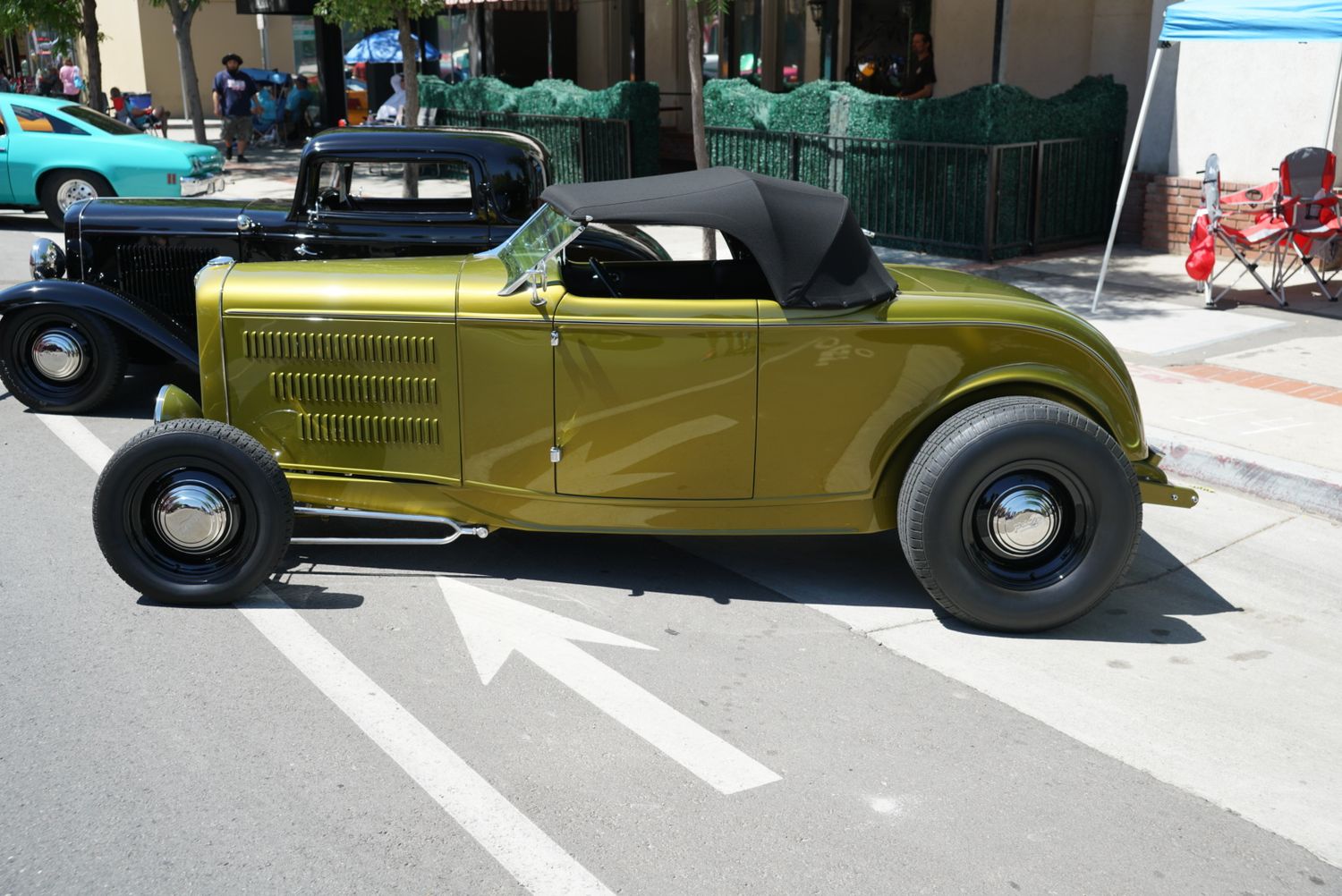 Gold 1932 Ford hot rod roadster on display at a classic car show on city street.