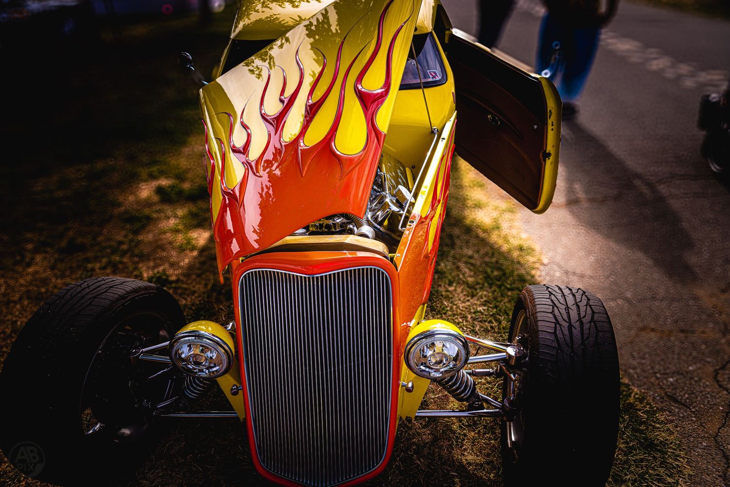Yellow and orange flame hot rod street rod with open engine bay at car show.