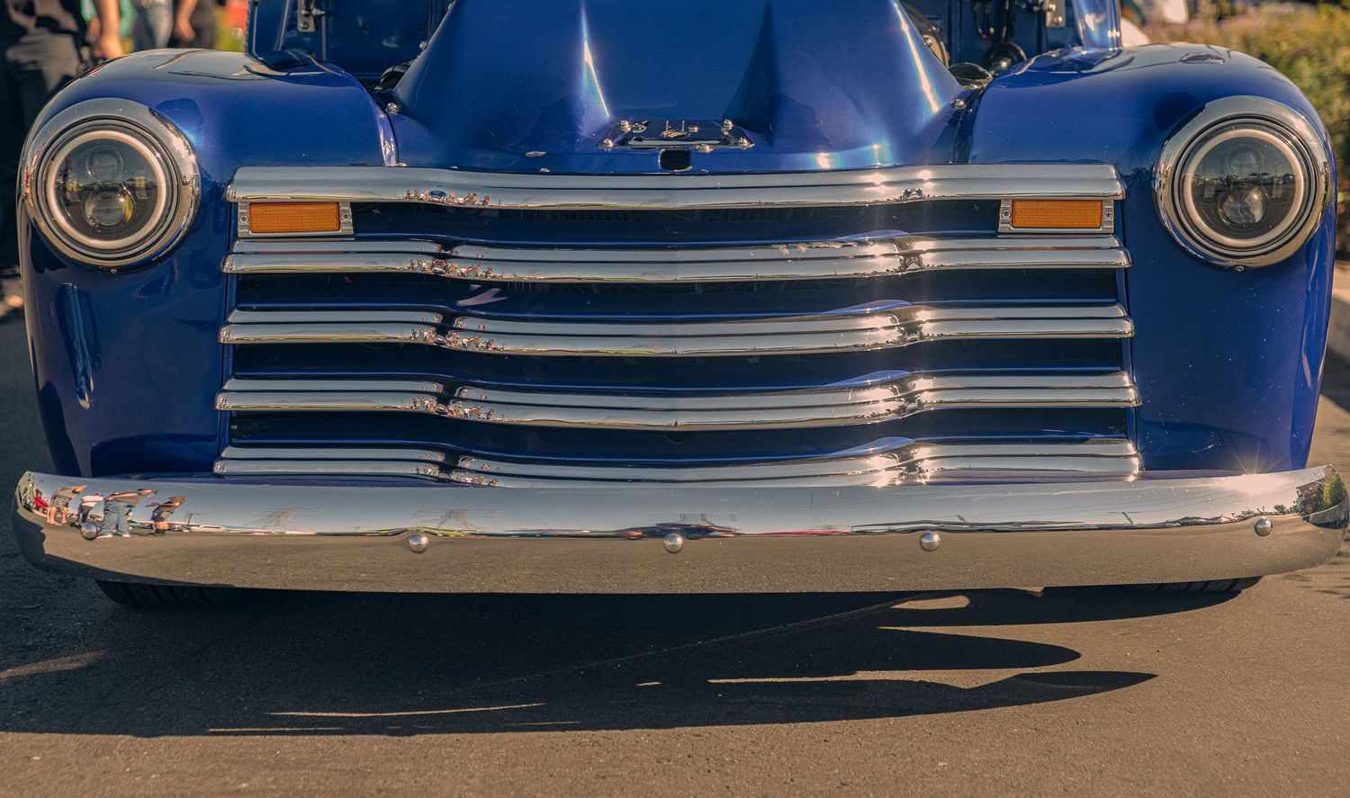 Front view of a restored blue classic Chevrolet truck with shiny chrome grille and round headlights.