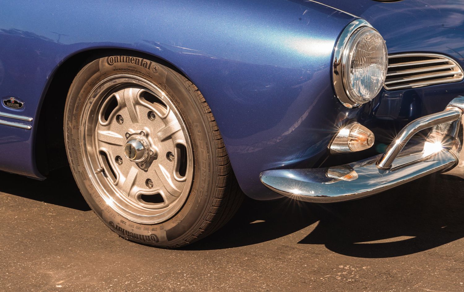 Close-up of a classic blue car showcasing a chrome wheel, Continental tire, and polished bumper on pavement.