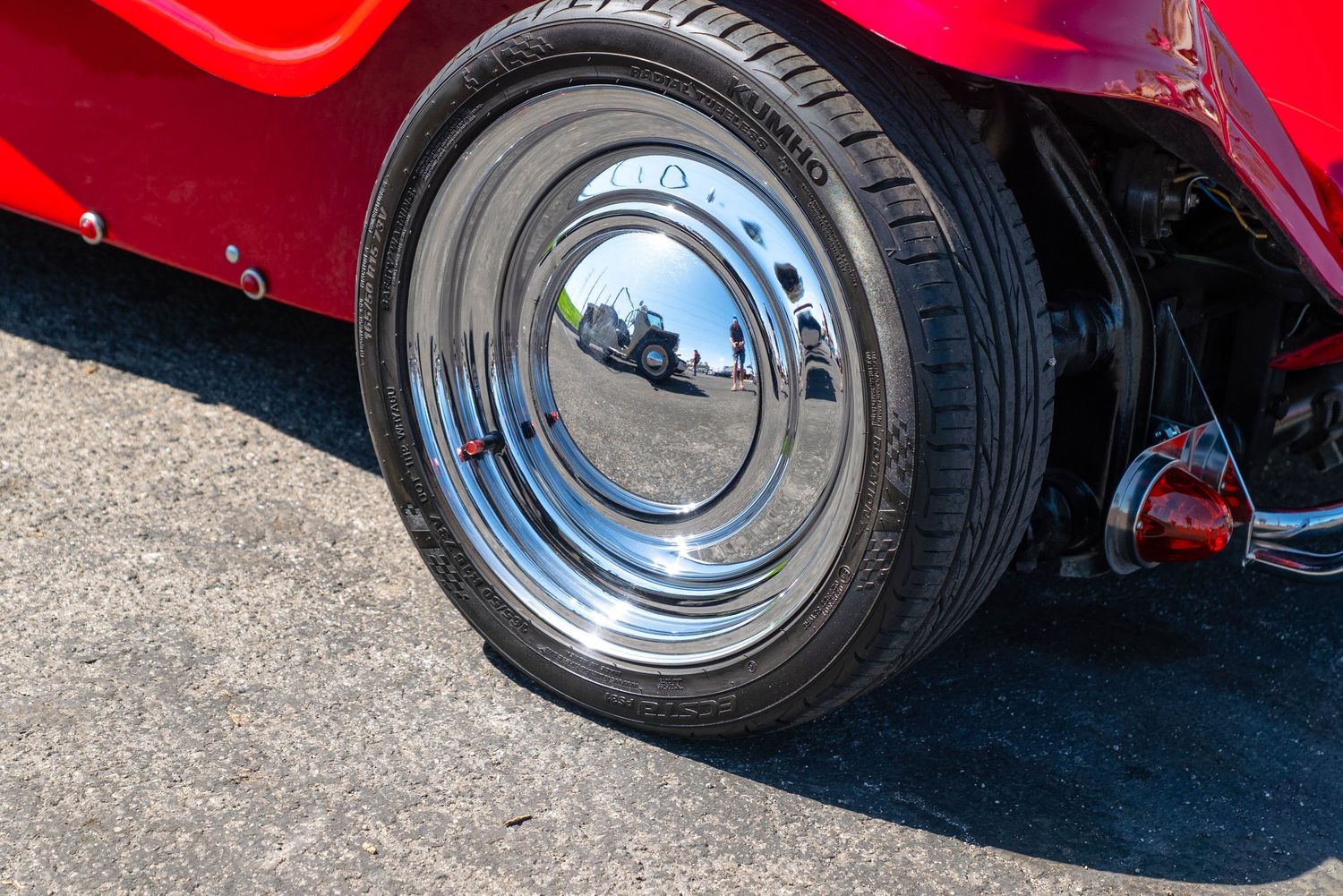 Polished chrome hubcap on a wide whitewall tire of a classic red hot rod at a car show.