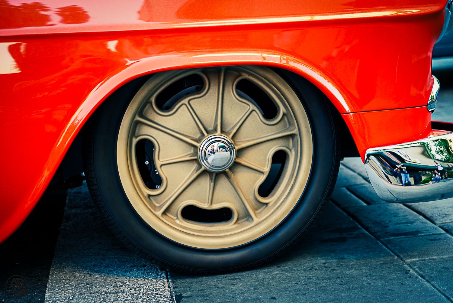 Close-up of a gold custom spoke wheel on a lowered red classic car at an auto show.