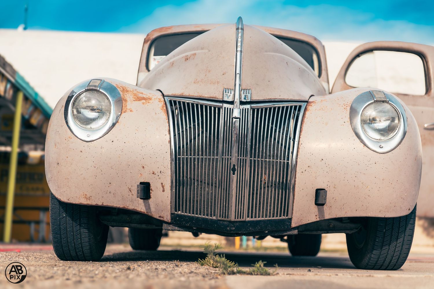Front view of a rusty vintage Ford classic car with chrome headlights and grille at an outdoor car show.