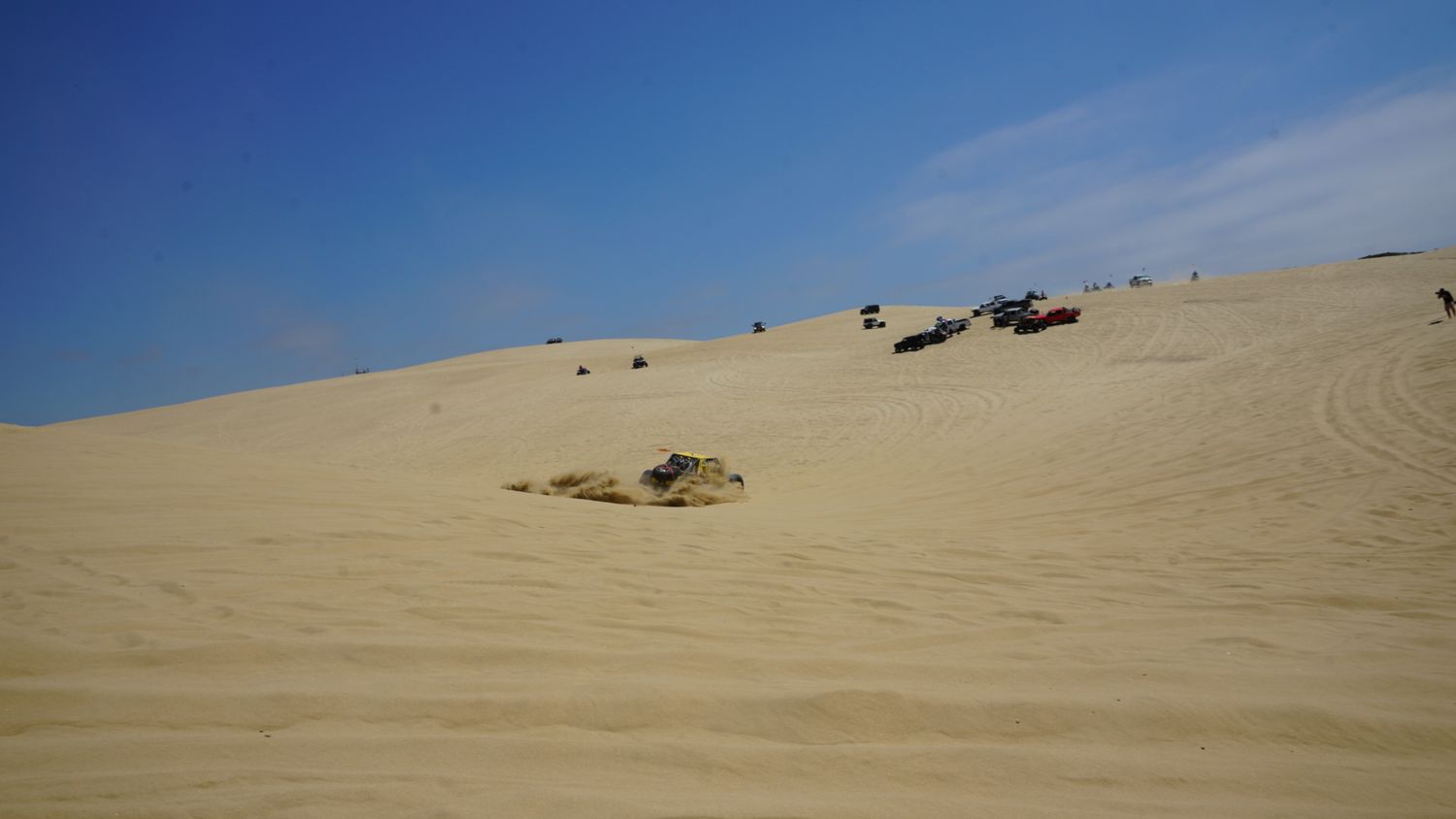 Overturned off-road vehicles resting on vast sandy desert dunes under a clear blue sky.