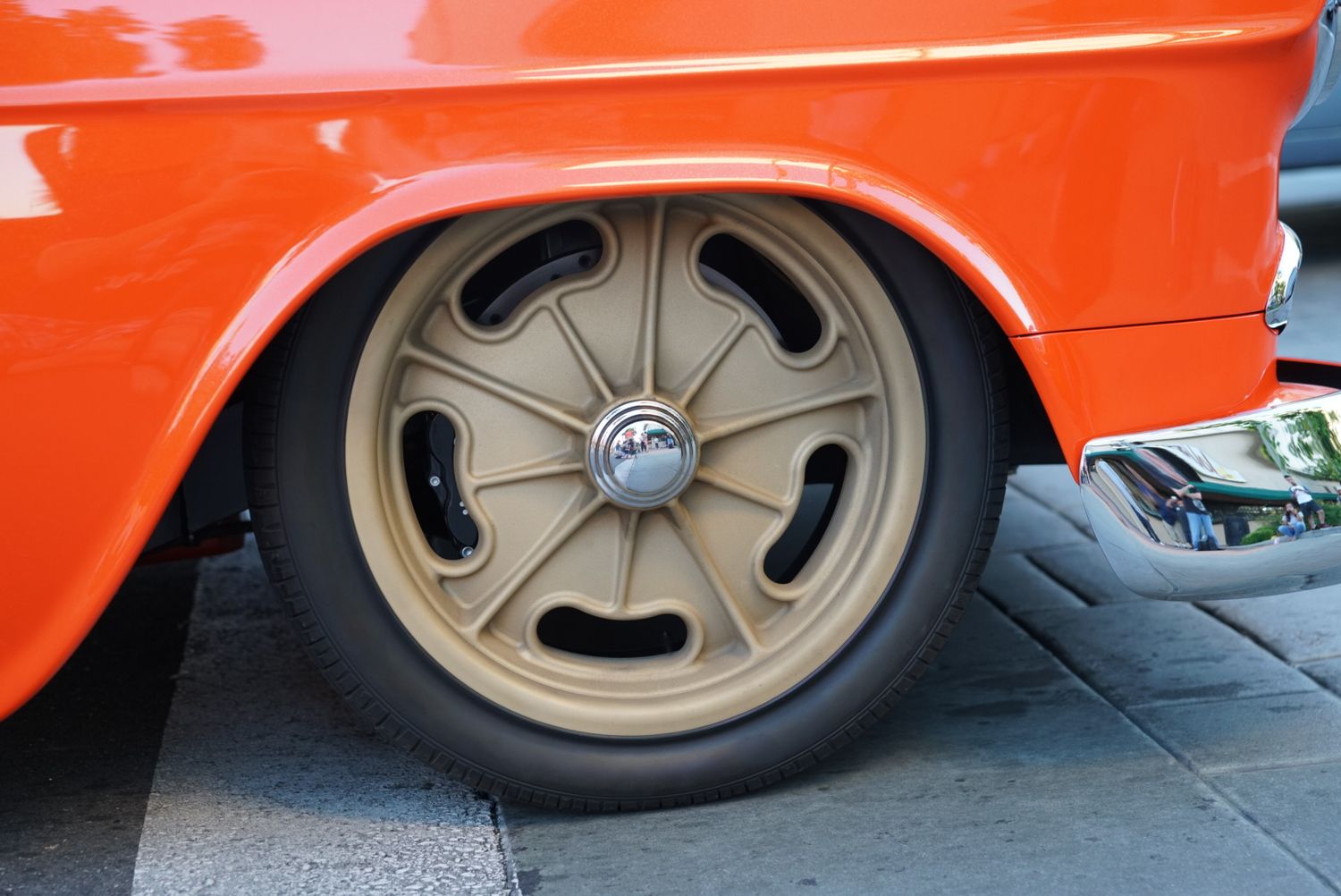 Classic orange hot rod with gold five-spoke drag racing wheel and wide slick tire.