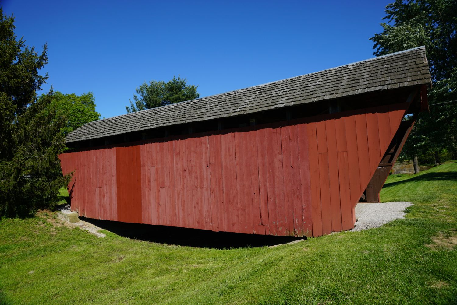 Classic red painted wooden covered bridge on green grass under a bright blue summer sky.