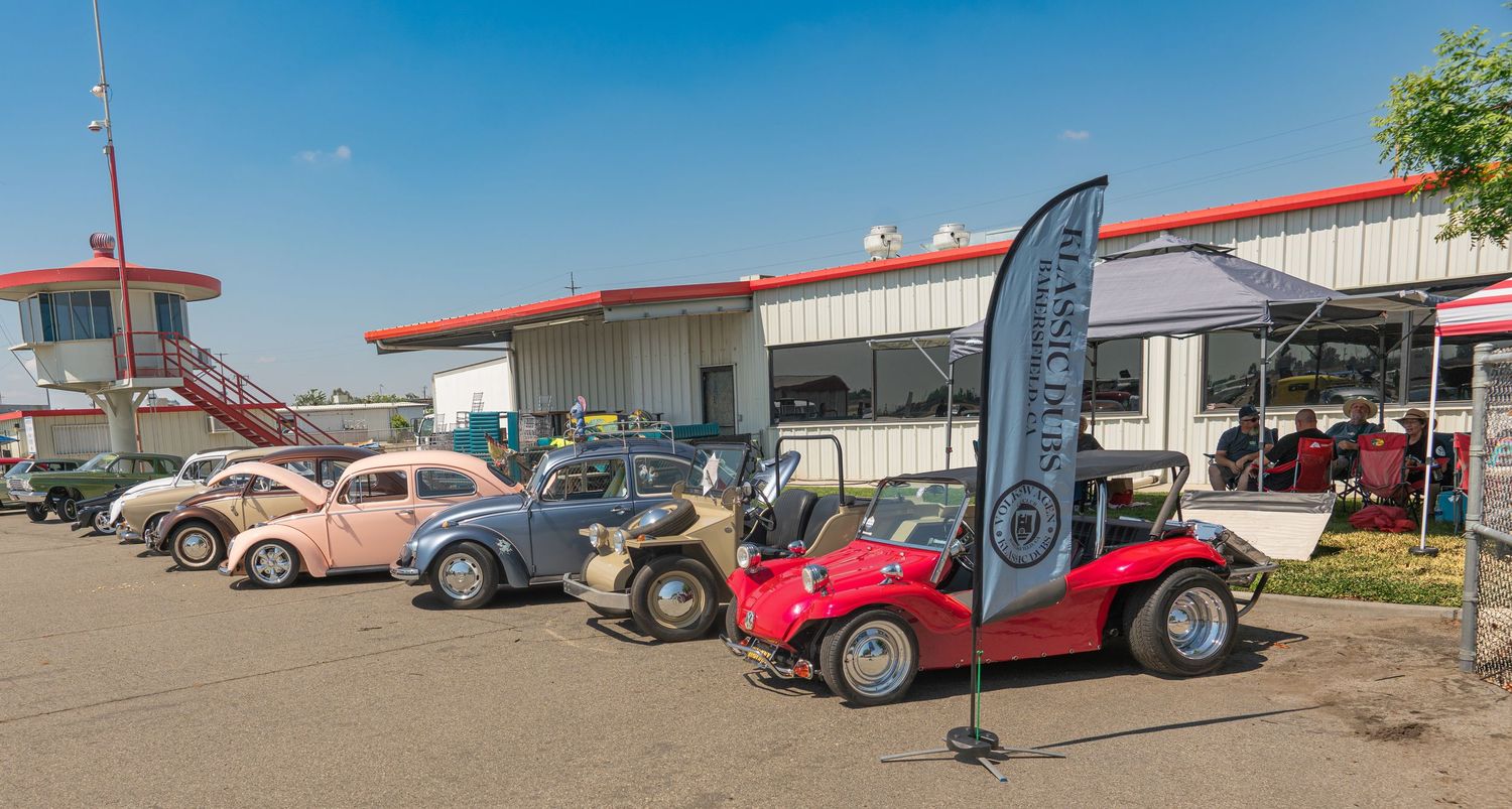 Vintage VW Beetles and a red dune buggy on display at an outdoor classic car show on a sunny day.