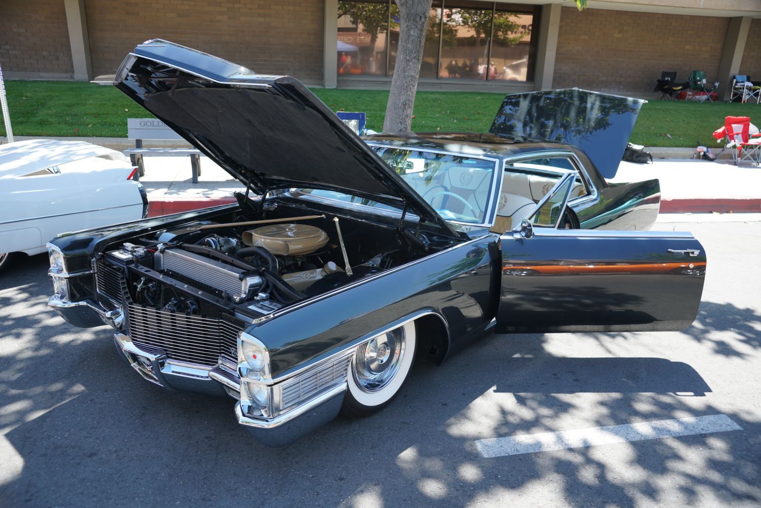 Classic black Cadillac vintage car with hood open displaying engine at outdoor car show.