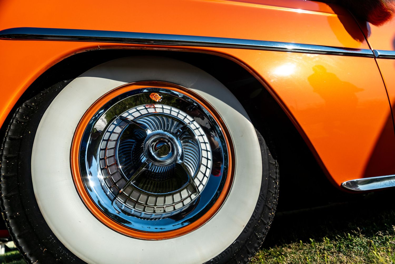 Classic orange car with chrome hubcap and white wall tire detail at vintage auto show.
