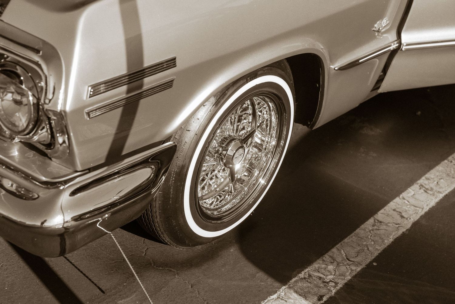 Sepia tone vintage lowrider classic car with whitewall tire and chrome wire wheel on pavement.