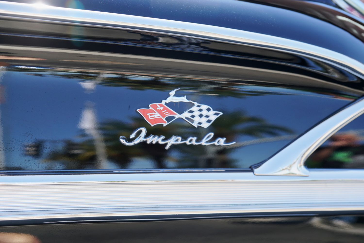Close-up of a classic Chevrolet Impala emblem with crossed flags logo on a vintage black car.