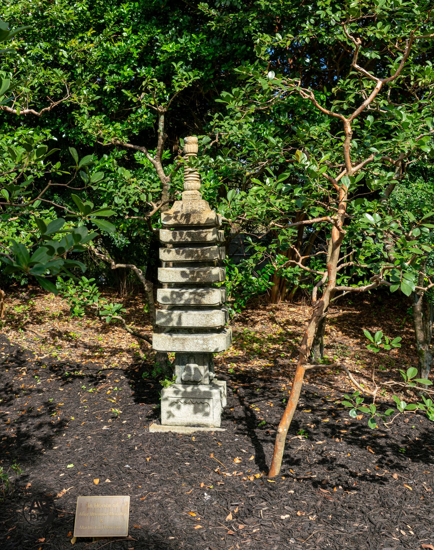 Ancient stone pagoda lantern sculpture surrounded by manicured bonsai trees in Japanese garden.