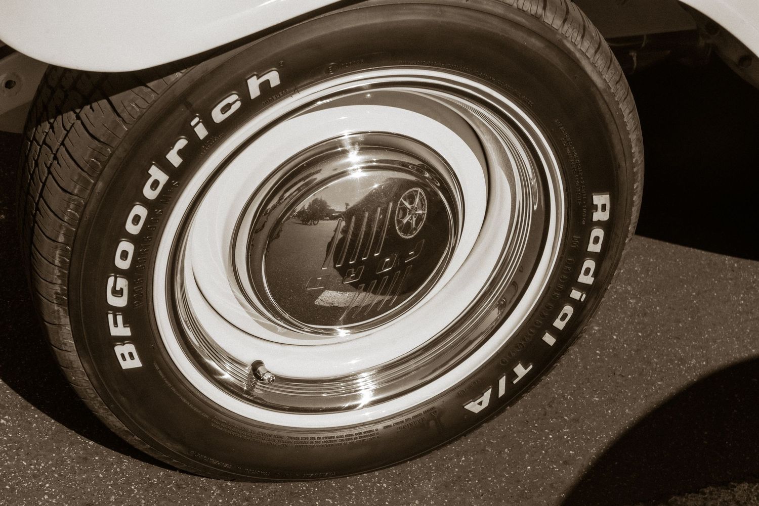 Sepia-toned close-up of a BFGoodrich Radial T/A whitewall tire on a classic car with chrome hubcap.