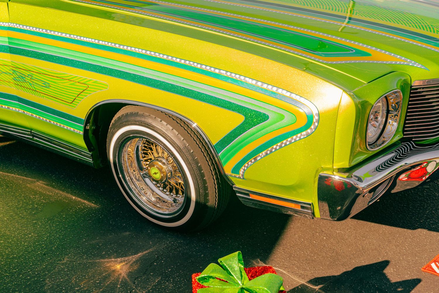 Close-up of a vibrant green and yellow lowrider car with custom paint, chrome wire wheels, and decorative striping.