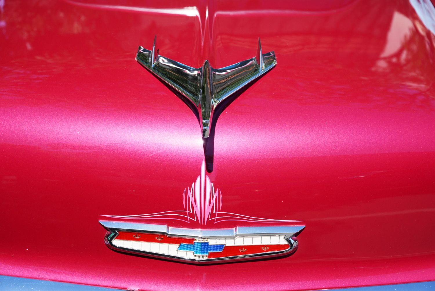 Close-up of a chrome Chevrolet hood ornament and emblem on a deep red classic car.