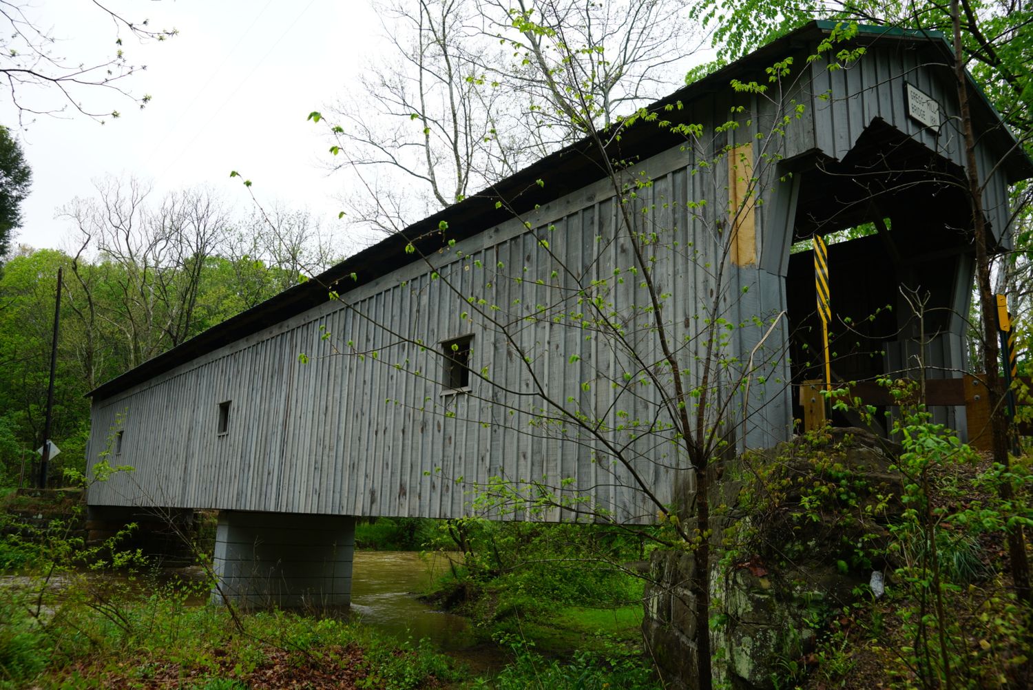 Long weathered gray wooden covered bridge spanning a creek amid autumn trees in Ohio.