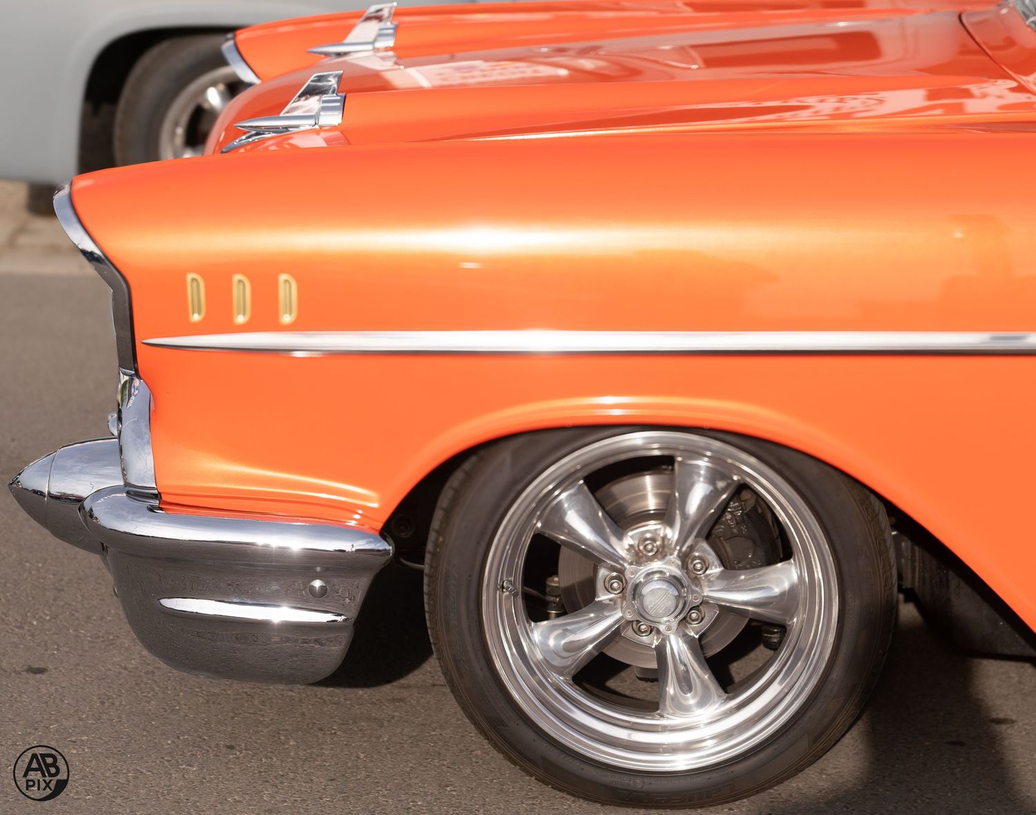 Close-up of an orange classic Chevrolet rear quarter panel with chrome trim and polished five-spoke wheel.
