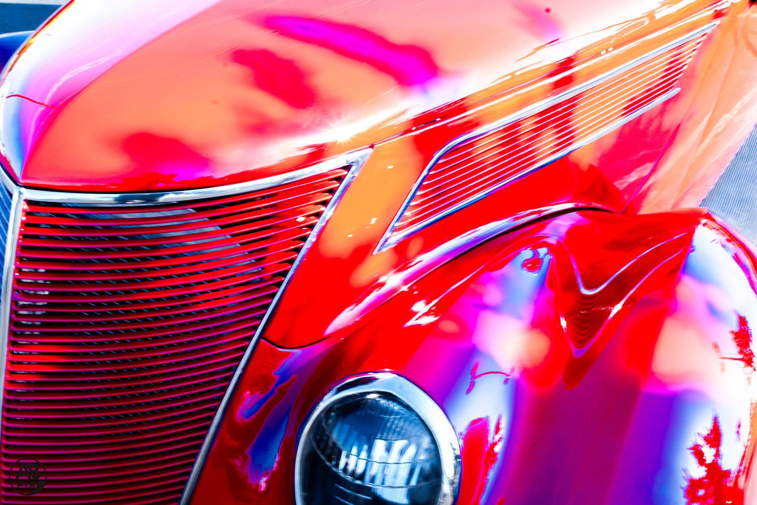 Abstract close-up of a glossy red classic car hood and grille with vivid reflections and chrome trim.