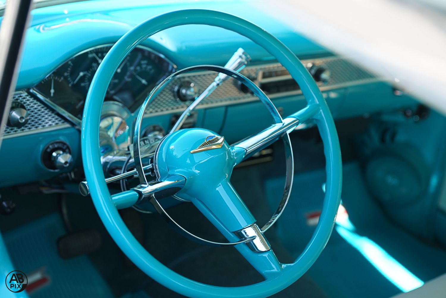 Turquoise vintage car interior featuring a classic steering wheel and chrome dashboard.