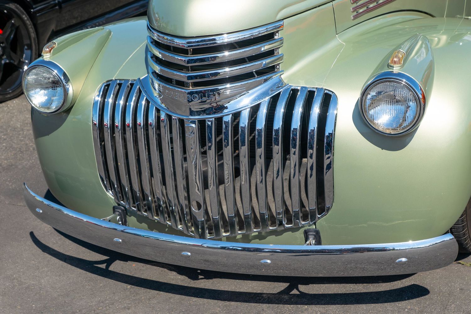 Close-up of a gleaming chrome vertical bar grille on a restored sage green 1941 Chevrolet at a car show.