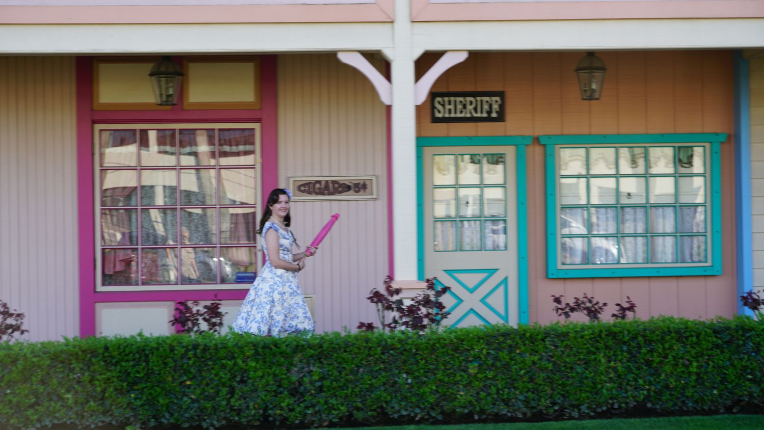 A woman in a vintage dress walks past colorful Sheriff building facades at a theme park.