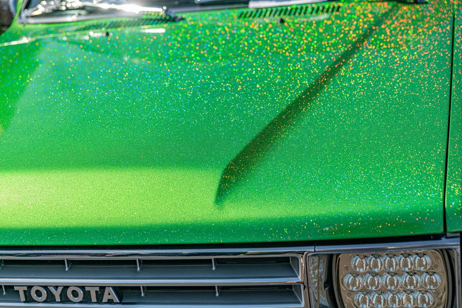 Close-up of a sparkling green metallic Toyota car hood with glitter paint finish and chrome grille detail.