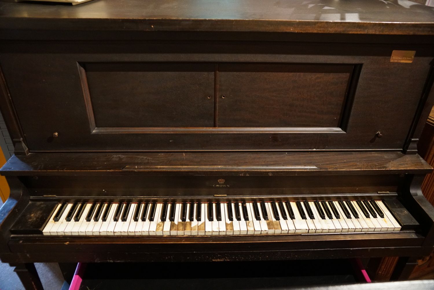 An antique dark wood upright piano with worn ivory and ebony keys sits against an interior wall.