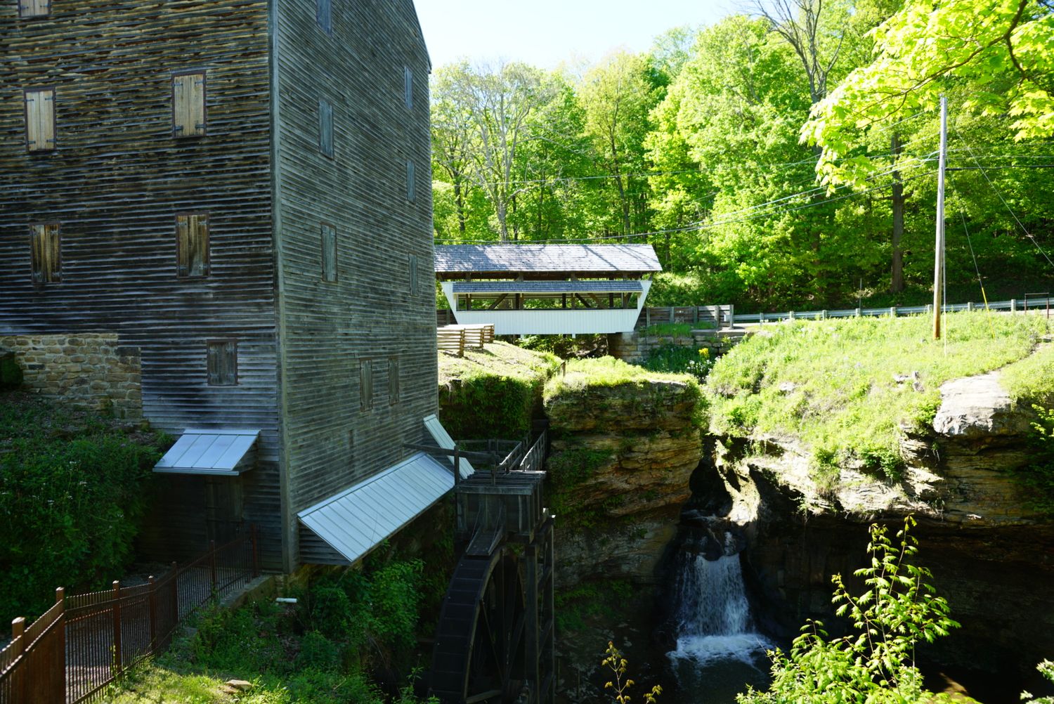 Historic stone grist mill with waterfall beside rocky cliff surrounded by lush green trees.