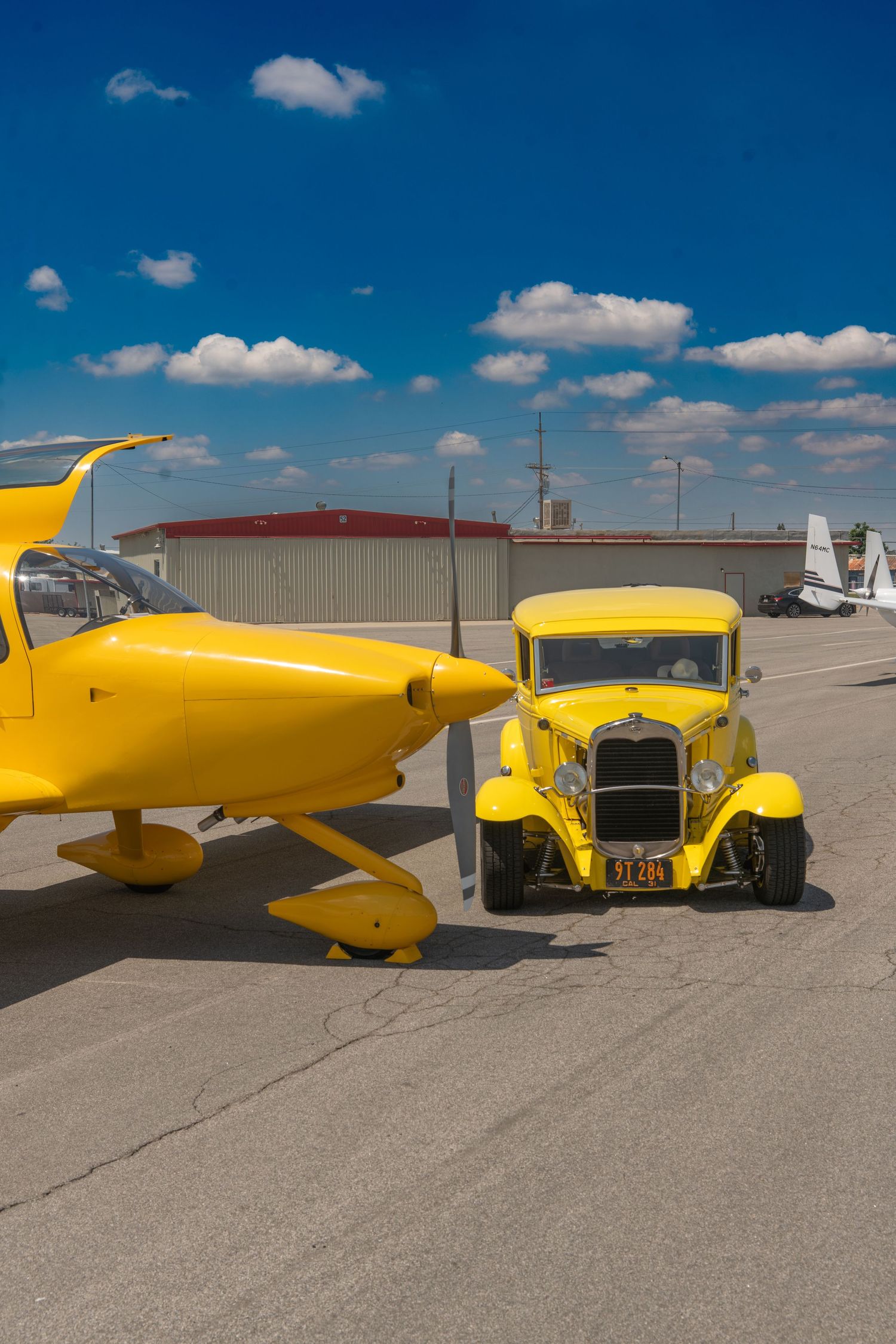 Matching yellow hot rod car and yellow propeller airplane parked side by side on an airport tarmac.