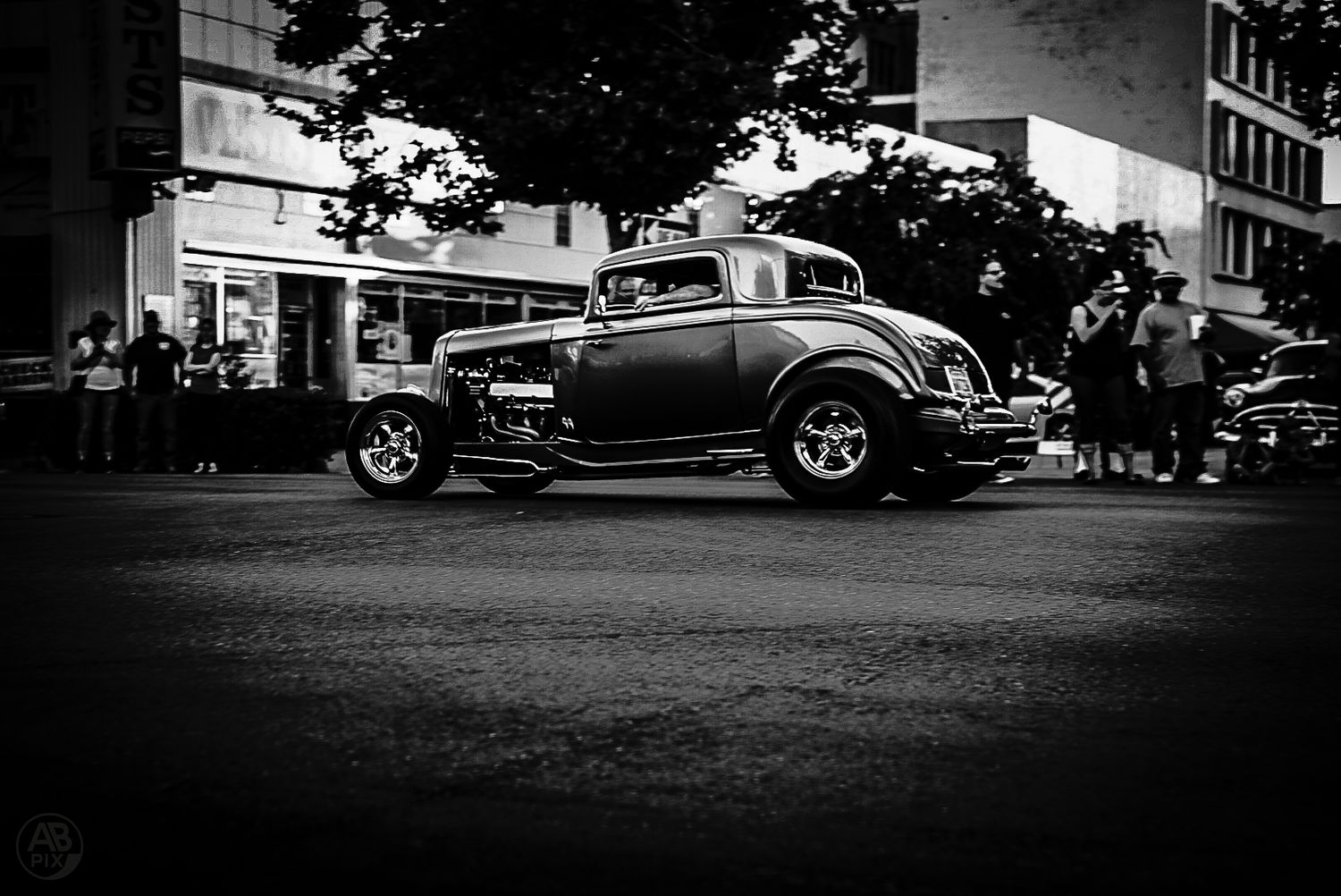 Black and white side profile of a classic hot rod coupe parked on a city street.