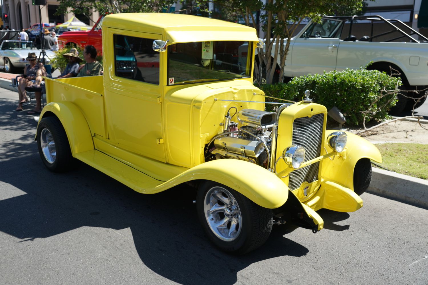 A bright yellow 1930s Ford hot rod pickup truck with exposed engine on display at a classic car show.